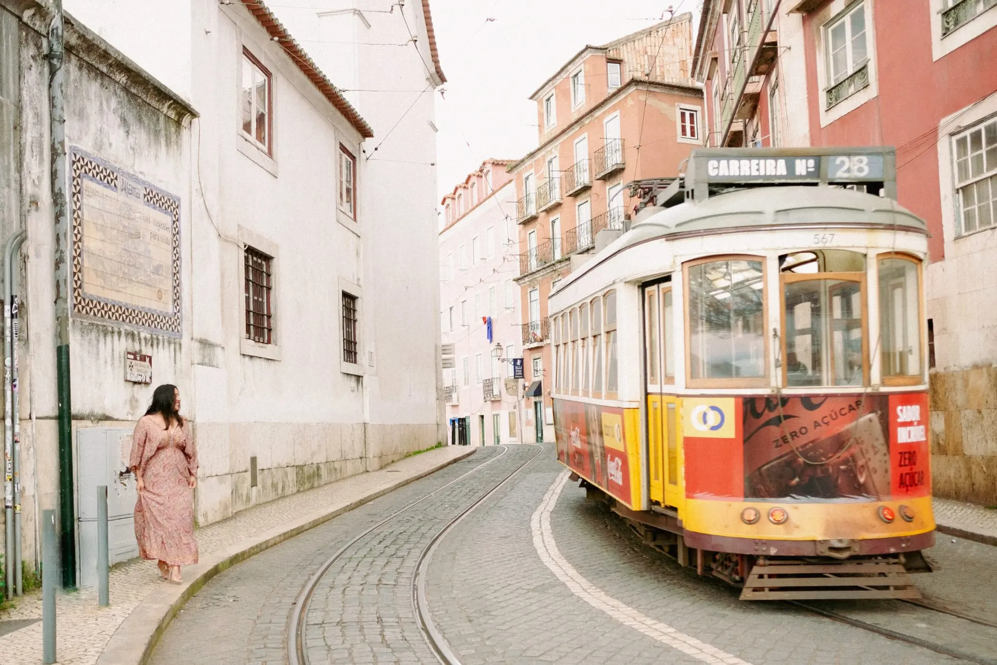 Jeannette Ceja walking a Lisbon street as the number 28 tram comes down it